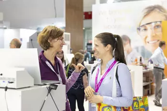Two women at a trade fair stand with analytcia lanyards are talking in front of an open laptop.