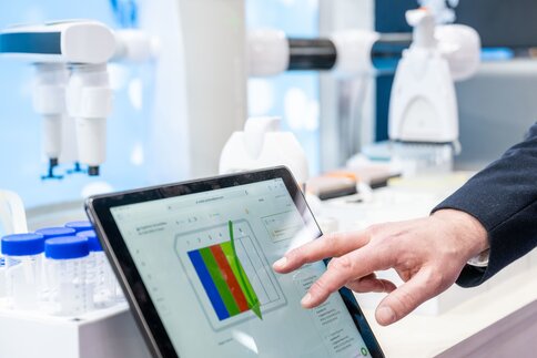 Eine Person bedient ein Tablet mit einer grafischen Auswertung in einem Laborumfeld.