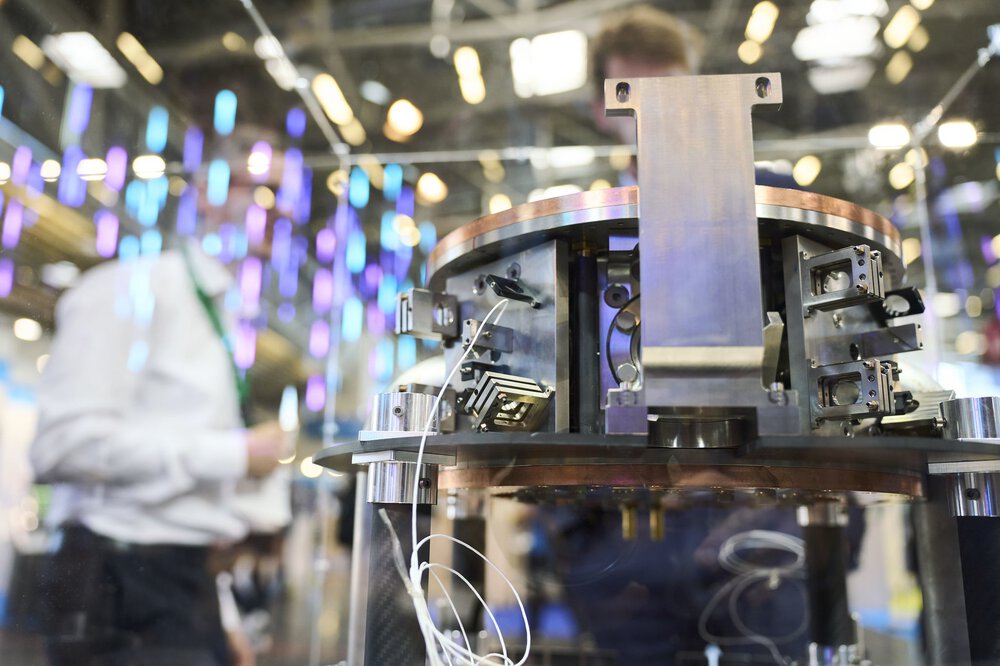Nahaufnahme einer wissenschaftlichen Ausrüstung mit Drähten, ausgestellt auf einer Technologieausstellung mit Menschen im Hintergrund.