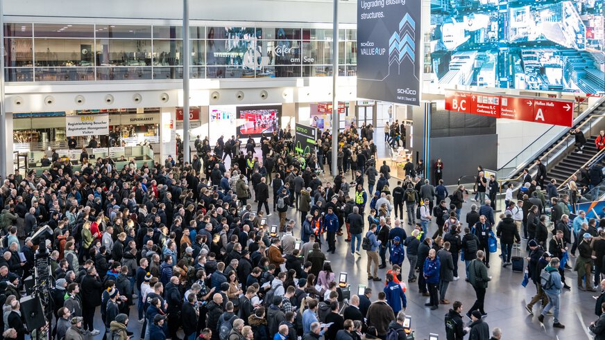 Blick über die Eingangshalle der BAU, in der zahlreiche Besucher vor den Einlasskontrollen warten, während weitere Besucher bereits hinter den Kontrollen stehen.