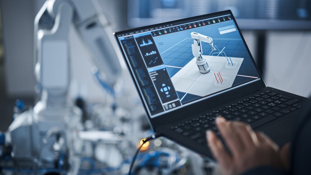 Hand einer Person mit Laptop zur Programmierung eines Roboterarms unter Einsatz fortschrittlicher Technologie wie KI