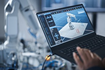 Hand einer Person mit Laptop zur Programmierung eines Roboterarms unter Einsatz fortschrittlicher Technologie wie KI