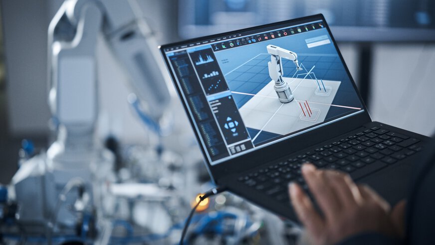 Hand einer Person mit Laptop zur Programmierung eines Roboterarms unter Einsatz fortschrittlicher Technologie wie KI