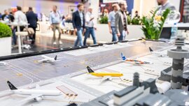 Model airplanes on an airport diorama with people walking and talking in the background at an event.