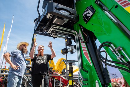 Zwei Männer stehen an einer großen grünen Maschine auf einer Outdoor-Ausstellung unter blauem Himmel.