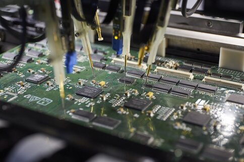 Close-up of a machine soldering electronic components onto a green circuit board.