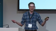 Eine Person im blau karierten Hemd hält einen Vortrag vor einer Leinwand.