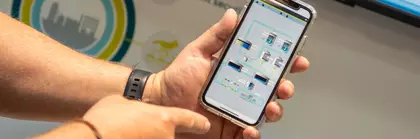 Person, die ein Smartphone hält auf dem ein Flussdiagramm für das im Hintegrund sichtbare Ausstellungsstück angezeigt wird.