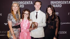 Three women and one man in festive attire stand smiling in front of a photo wall of the INHORGENTA AWARD, holding a trophy.