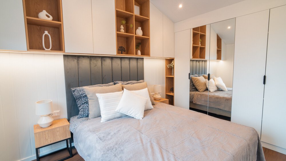 Ein großes Schlafzimmer mit Spiegelschränken und hohen hölzernen Hängeregalen über dem Kopfteil des Doppelbetts.