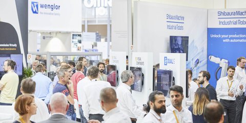 Gut besuchte Messehalle mit Menschen an verschiedenen Technologieständen.