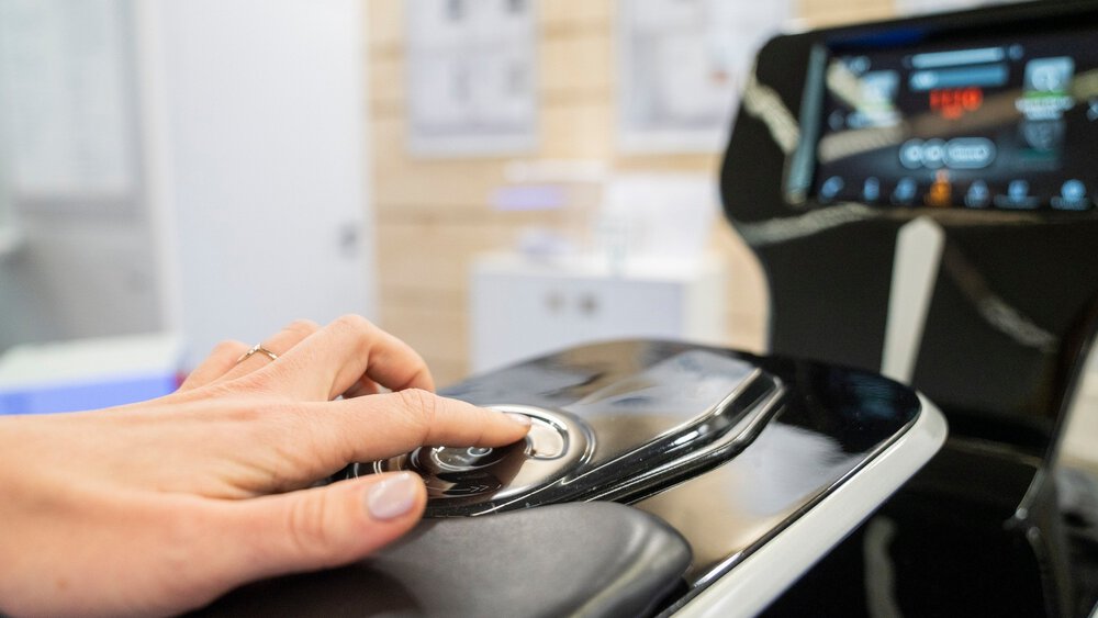 A person's hand presses a button on a modern control panel with a digital display in the background.