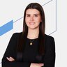 Auf dem Bild sieht man eine Frau mit einem Blazer mit verschränkten Armen auf einem weißen Hintergrund mit blauen Elementen