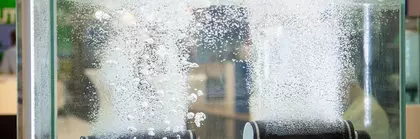 Bubbles rise from three different pipes in a glass box filled with water.