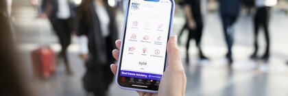 Person hält ein Smartphone, auf dessen Bildschirm die EXPO REAL App mit Event-Features angezeigt wird.