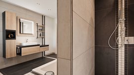 Modernes Badezimmer mit begehbarer Dusche, wandmontiertem Waschbecken, großem Spiegel und minimalistischen Holzregalen.