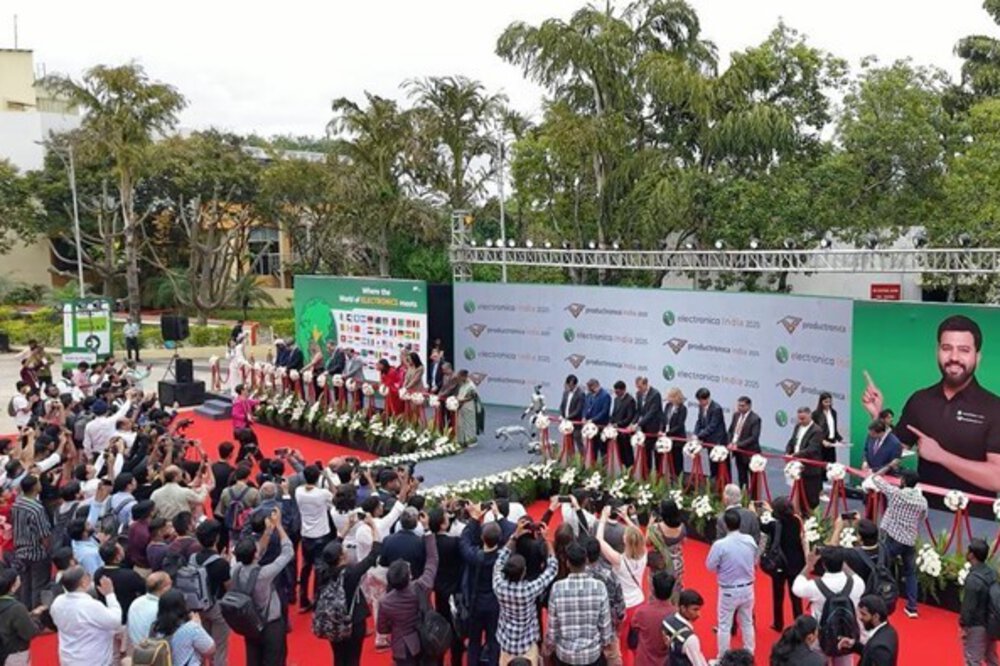A crowd participates in an outdoor ribbon-cutting ceremony while officials stand on stage and photographers capture the event.