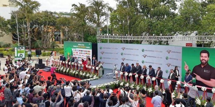 A crowd participates in an outdoor ribbon-cutting ceremony while officials stand on stage and photographers capture the event.