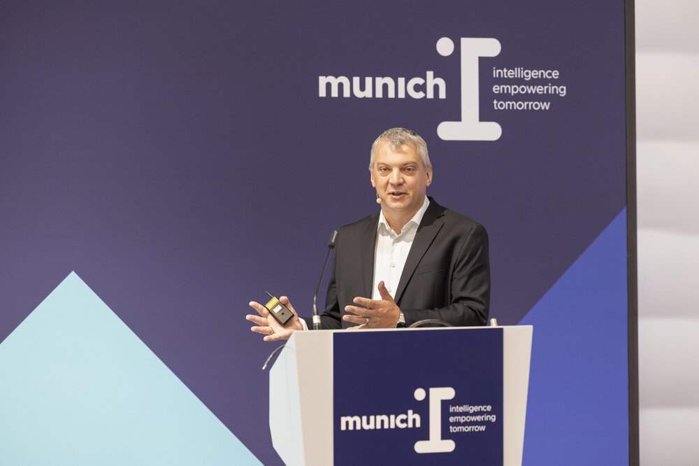 A man in a suit and with grey hair gives a lecture on a podium at ‘munich i’.