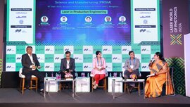 Two women and three men are sitting on a stage at Laser World of Photonics India. Behind them is a screen displaying information about the speakers.