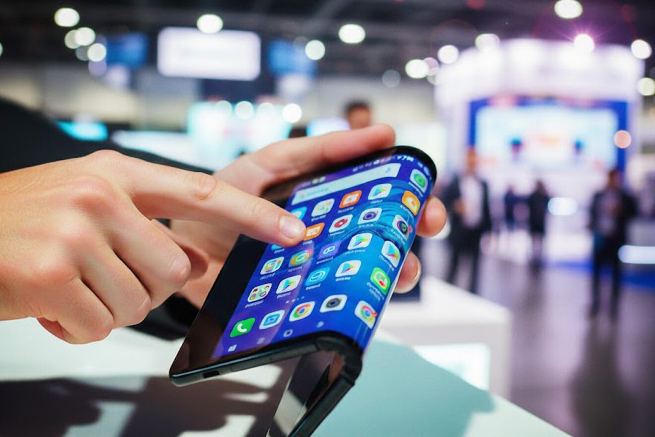 Auf dem Bild kann man einen Tablet Bildschirm sehen, der in der Mitte gefaltet ist, er wird von einer Männerhand auf einer Messe gehalten.