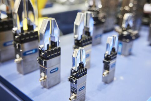 Several industrial robot grippers are displayed upright on a blue surface in a well-lit environment.