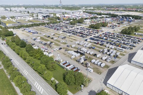 Luftaufnahme des großen Parkplatzes voller Autos und Wohnmobile vor dem Messeeingang Ost. Im Hintergrund sind die Messehallen zu sehen.