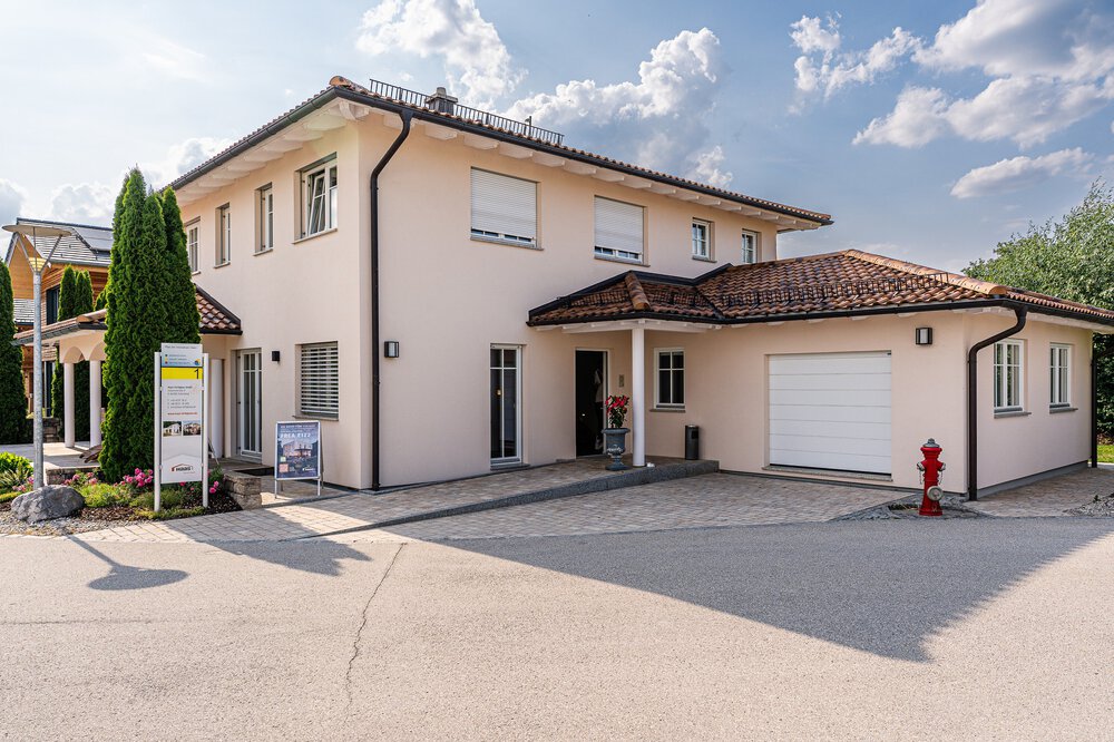 Modernes zweistöckiges Haus mit beigen Wänden, braunem Dach, Garage und einem roten Hydranten davor. Darüber bewölkter Himmel.