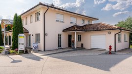 Modernes zweistöckiges Haus mit beigen Wänden, braunem Dach, Garage und einem roten Hydranten davor. Darüber bewölkter Himmel.