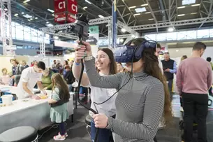 Person, die ein VR-Headset und einen Controller bei einer Indoor-Veranstaltung mit Personen im Hintergrund verwendet.