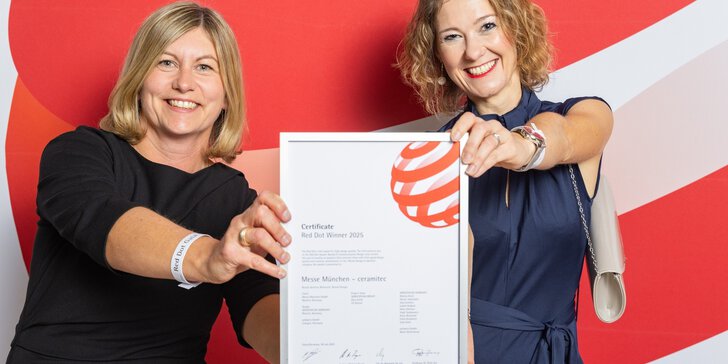 Two smiling women in formal attire hold up ceramitec's “Red Dot Winner 2025” certificate for the camera.