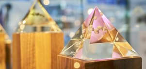 An exhibit, a glass pyramid in which shapes can be recognized on a wooden base, presented in front of a blurred background.