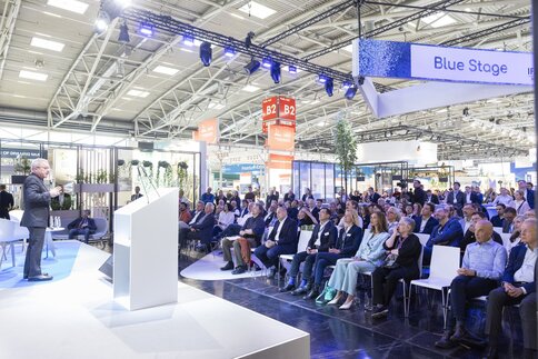 A speaker gives a presentation to a seated audience on the IFAT Munich Blue Stage.