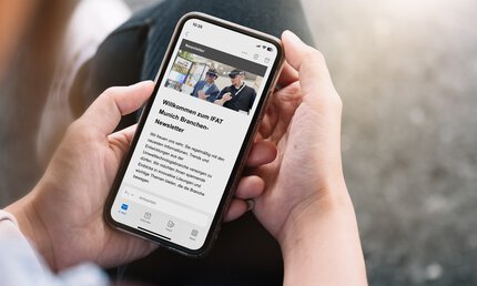 Eine Person hält ein Handy, auf dessen Display der Branchen-Newsletter der Messe IFAT Munich erscheint