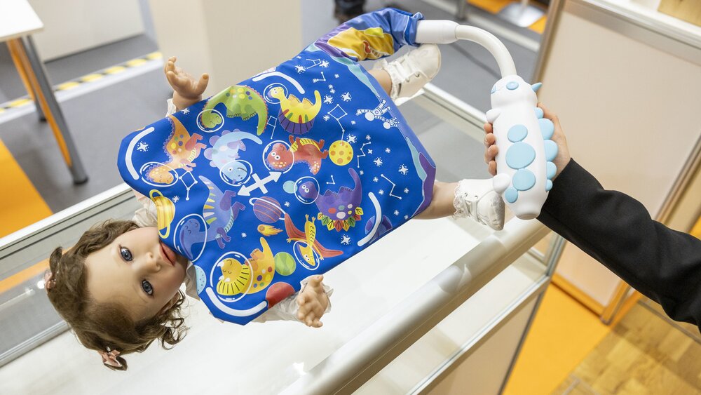 Close-up of a baby doll on a display area covered with a colourful dinosaur blanket that can be inflated with a hand pump.