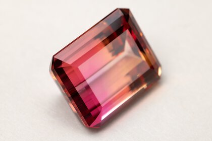 The close-up view of a rectangular cut gemstone in several shades of red resting on a white surface.