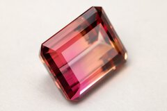 The close-up view of a rectangular cut gemstone in several shades of red resting on a white surface.