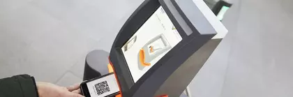 Several ticket scanners in the entrance area of productronica. A person holds their smartphone with a QR code ticket under the device.
