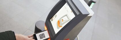 Several ticket scanners in the entrance area of productronica. A person holds their smartphone with a QR code ticket under the device.