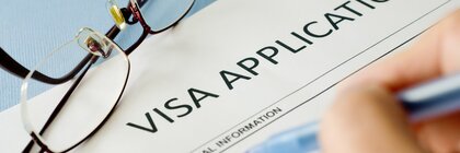 A hand is filling out a visa application form. Glasses lie next to it.