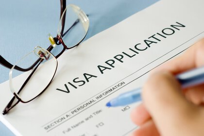 A hand is filling out a visa application form. Glasses lie next to it.
