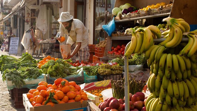 Ein Mann wählt an einem Marktstand im Freien Obst und Gemüse aus.