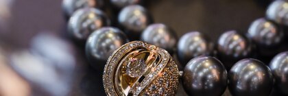 Close-up of a luxurious pearl necklace with a round diamond-studded pendant on a dark surface.