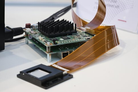 Electronic module with connected ribbon cable, connected to an optical component – part of a device for integrated photonic chips.
