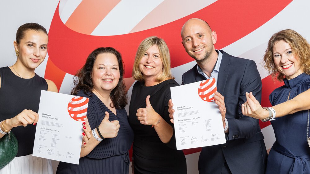 Fünf Menschen lächeln, halten Urkunden in der Hand und zeigen den Daumen nach oben vor einem rot-weißen Hintergrund.