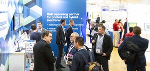 Menschen unterhalten sich an einem LOPEC Messestand mit blauem Hintergrund und Informationsmaterialien.