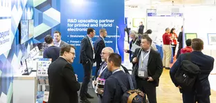 Menschen unterhalten sich an einem LOPEC Messestand mit blauem Hintergrund und Informationsmaterialien.