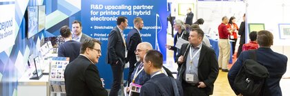 People talking at a LOPEC booth with blue background and information materials.