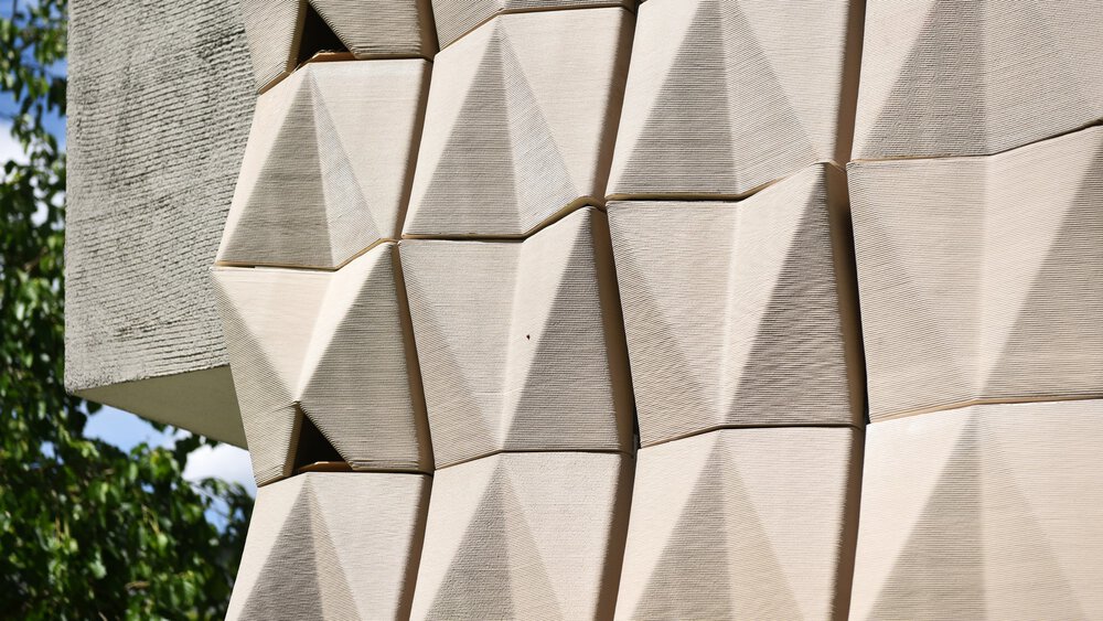 Geometric beige tiles with angular patterns form a modern wall, with a green area visible on the left-hand side.