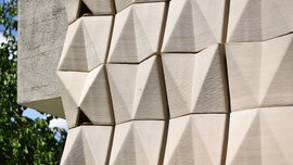 Geometric beige tiles with angular patterns form a modern wall, with a green area visible on the left-hand side.